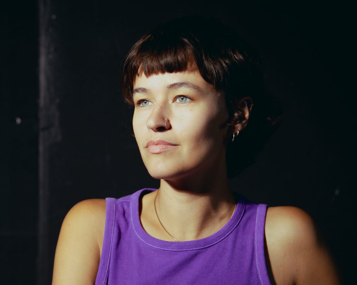 Portrait of Alma Akaya in a purple top, looking to the side in warm light